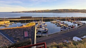 A harbor with boats docked, a stone wall, and a view of the sea and distant buildings. - The Beaches, beachfront 2 bed home with seaviews in Banff Aberdeenshire (Banff)