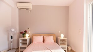 Une chambre à coucher avec un lit, des tables de chevet, un ventilateur sur pied et une fenêtre.