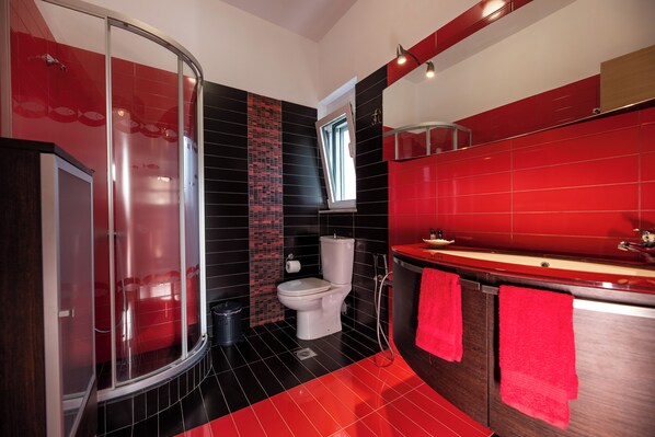 Un baño moderno con cabina de ducha de vidrio, inodoro y tocador con toallas rojas.
