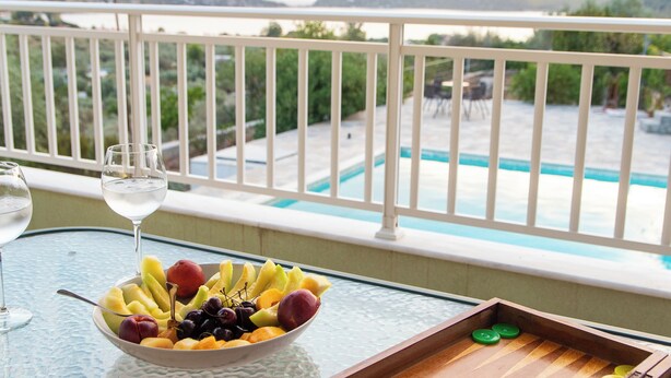 Un balcon avec vue sur la piscine, un saladier rempli de fruits et deux verres d’eau.