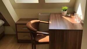 A small, well-lit attic bedroom with two skylights, a wooden desk, a chair, a radiator, and a potted plant. - Rentumi Hostel Świnoujście Noclegi (Swinoujscie)