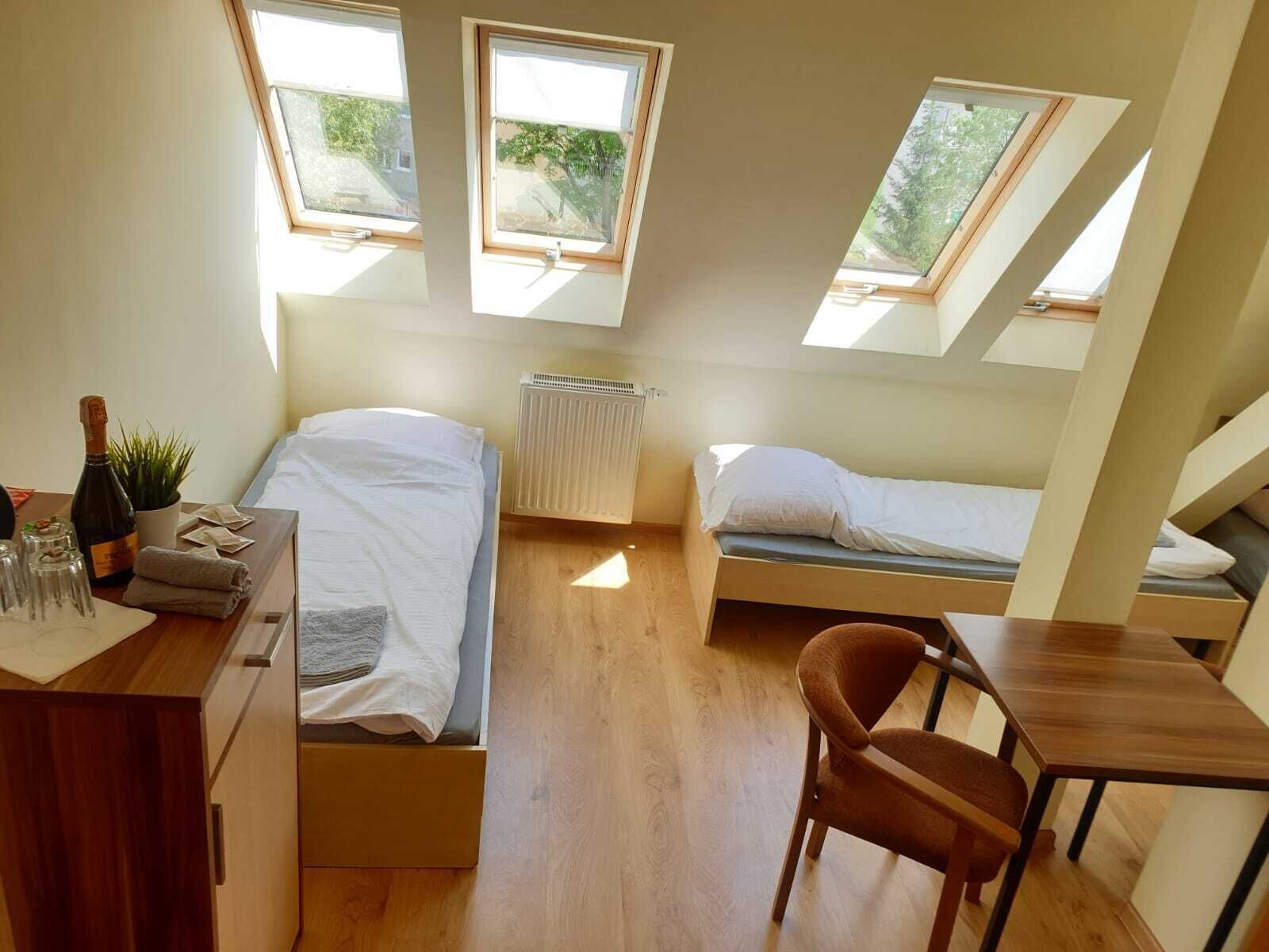 Une chambre de taille modeste, équipée de deux lits, d’un bureau et d’une chaise. Des fenêtres de toit permettent à la lumière naturelle d’entrer.