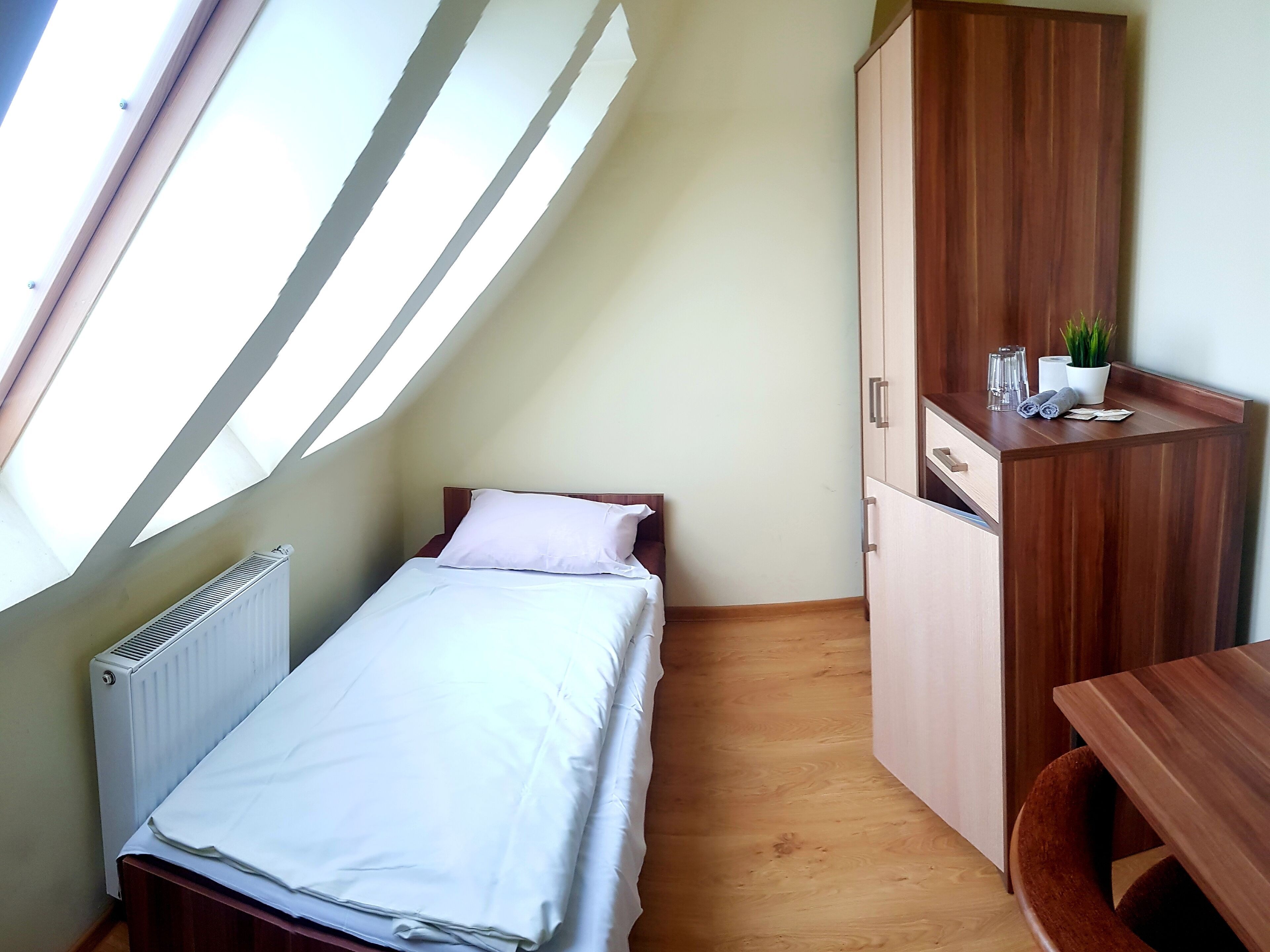 Ein kleines Zimmer mit einem Einzelbett, einem Holzschrank und einem Schreibtisch.