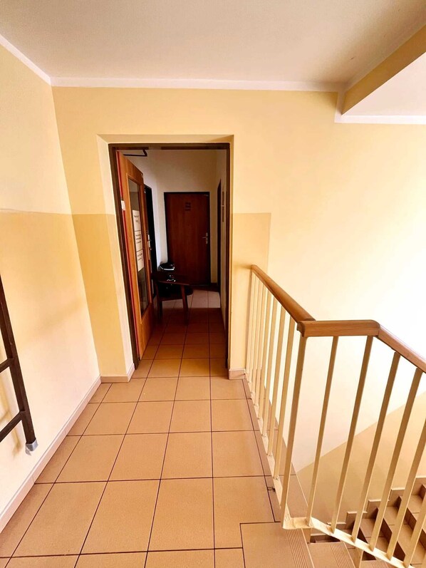 A corridor with tiled flooring, a wooden railing, and a door at the end leading to a room. - Rentumi Hostel Świnoujście Noclegi (Swinoujscie)