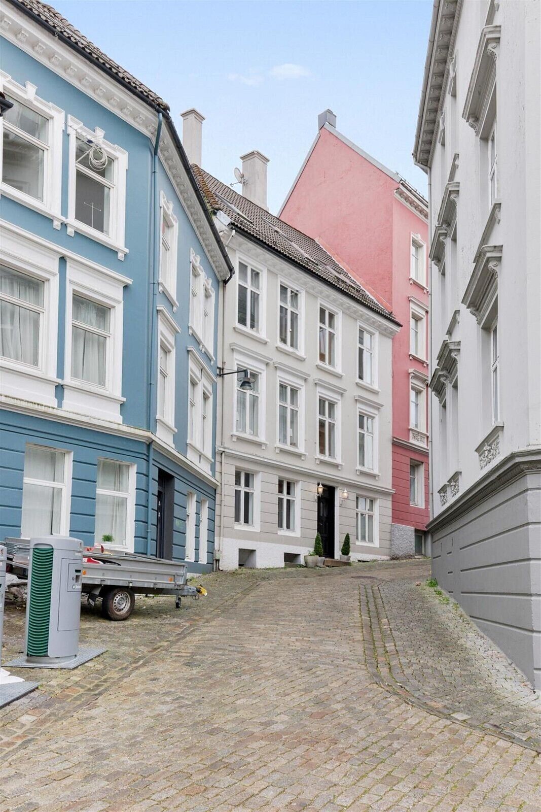 A narrow cobblestone street lined with multi-story buildings, some with visible balconies and windows.