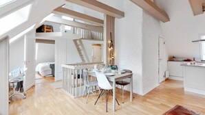 A spacious loft with a high ceiling, exposed wooden beams, a dining area with a table and chairs, a kitchen area, and a staircase leading to an upper level. - Urban Apartment - City Center (Bergen)