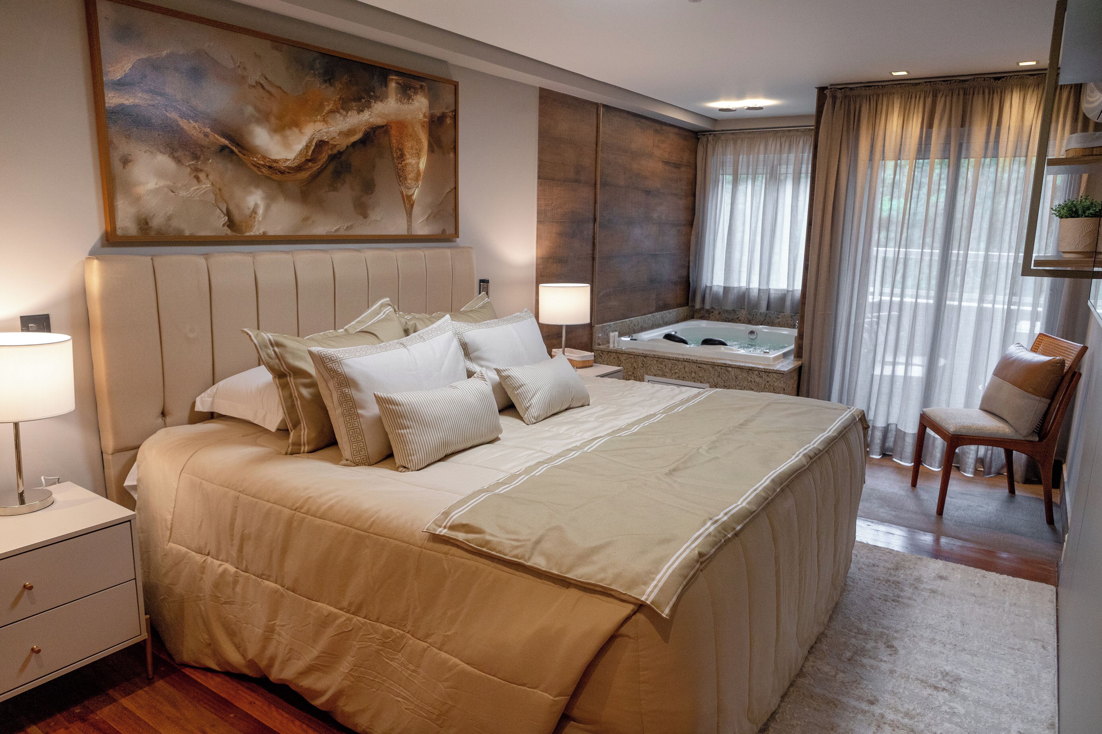Amplia habitación con una cama grande, un espacio de descanso con una silla, una bañera y un cuadro abstracto de gran tamaño en la pared.