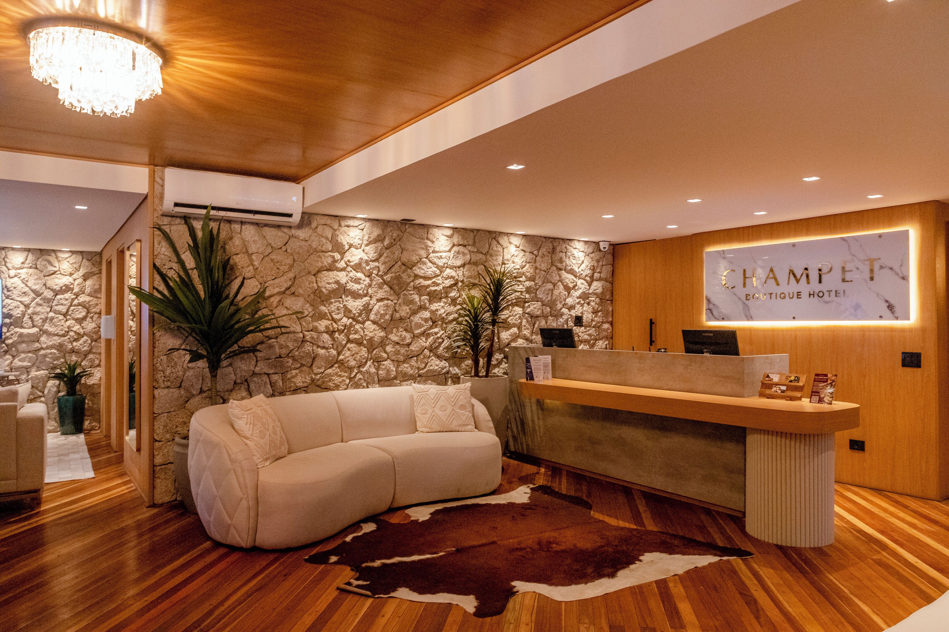 A hotel reception area with a stone wall, a reception desk, a sofa, and a chandelier.