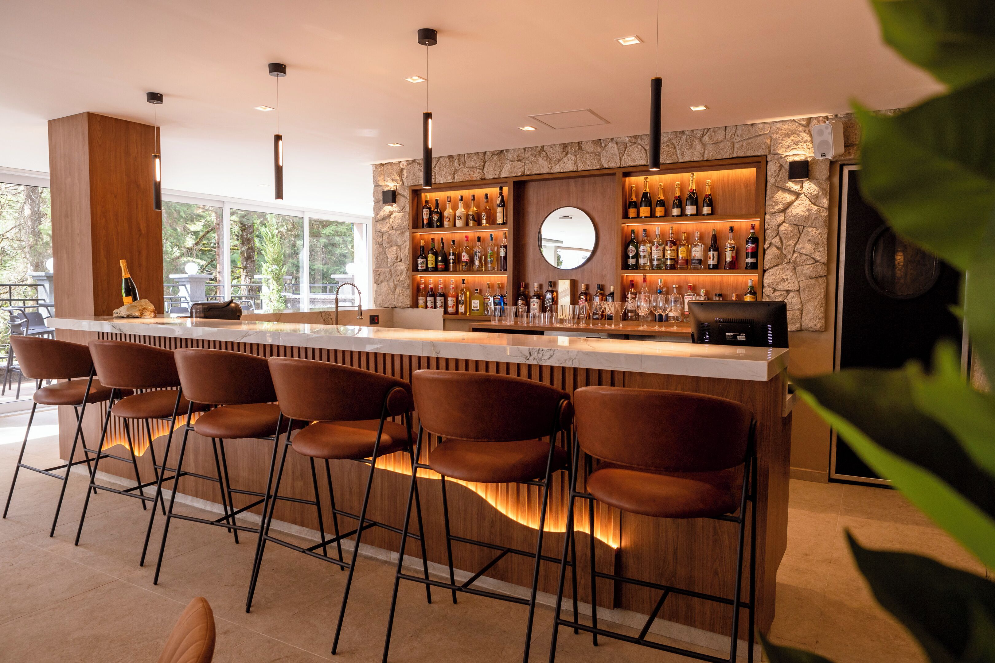Eine moderne Bar mit Marmorplatte, mehreren Barhocker und einer Auswahl an Flaschen.