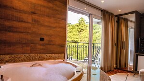 Ein modernes Badezimmer mit einer großen Badewanne, einer gläsernen Duschkabine und Blick auf einen Balkon mit Sitzmöbeln.