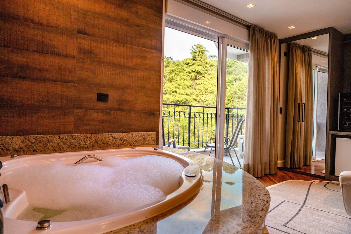 A modern bathroom with a large bathtub, a glass-enclosed shower area, and a view of a balcony with outdoor furniture.