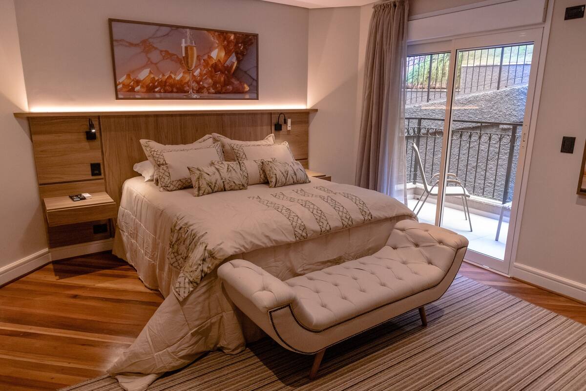 A bedroom with a large bed, a bench, a nightstand, and a sliding glass door leading to an outdoor area.