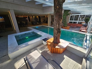 Un espace piscine comprenant deux piscines distinctes, des chaises longues et un tronc dâarbre servant dâĂ©lĂ©ment dĂ©coratif central.