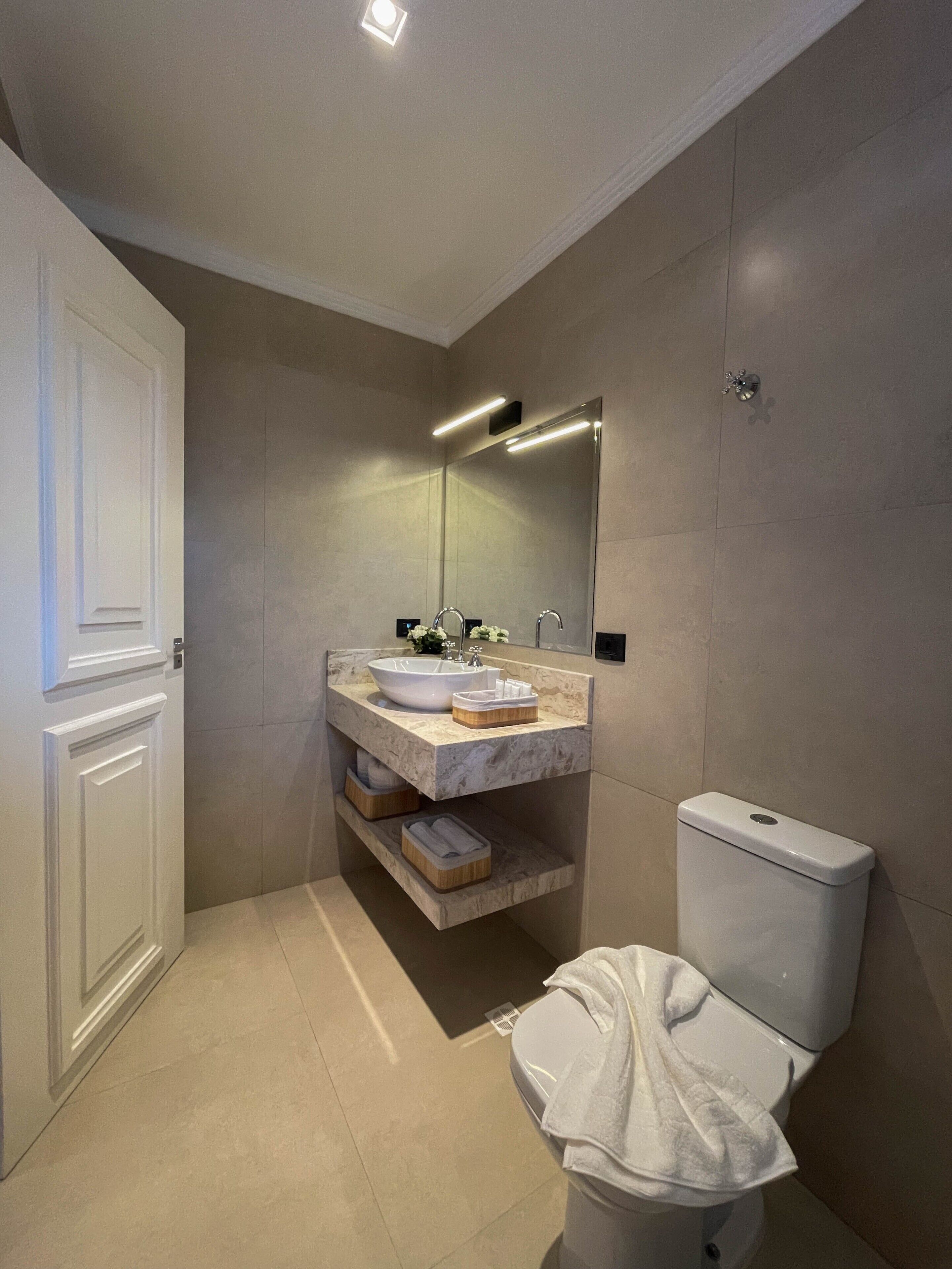 A modern bathroom with a white toilet, a marble sink, and a large mirror.