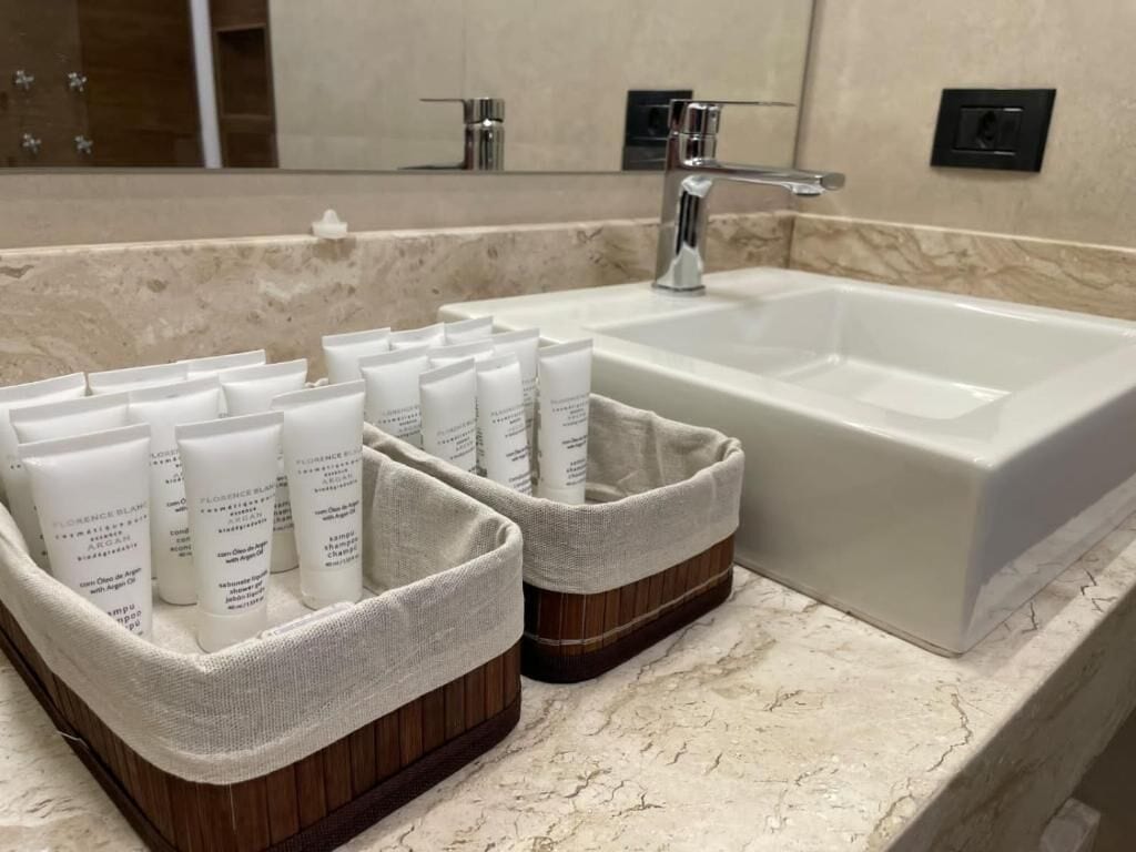 A bathroom with a large white bathtub, two beige baskets with toiletries, and a marble countertop.