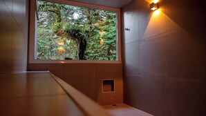A room with a window overlooking a forest, a bench, and a wall-mounted light fixture. - Champet Boutique Hotel (Campos do Jordão)