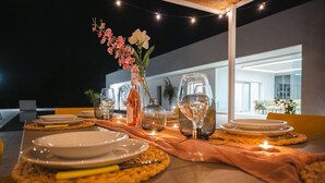 Een buiten eethoek met een tafel voor twee personen, inclusief borden, bestek en een vaas met bloemen.