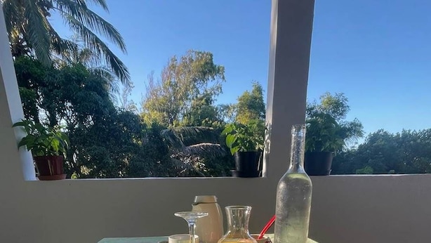 Ein Esstisch mit Frucht, Brot und Saft auf einem Balkon mit Blick auf Bäume.