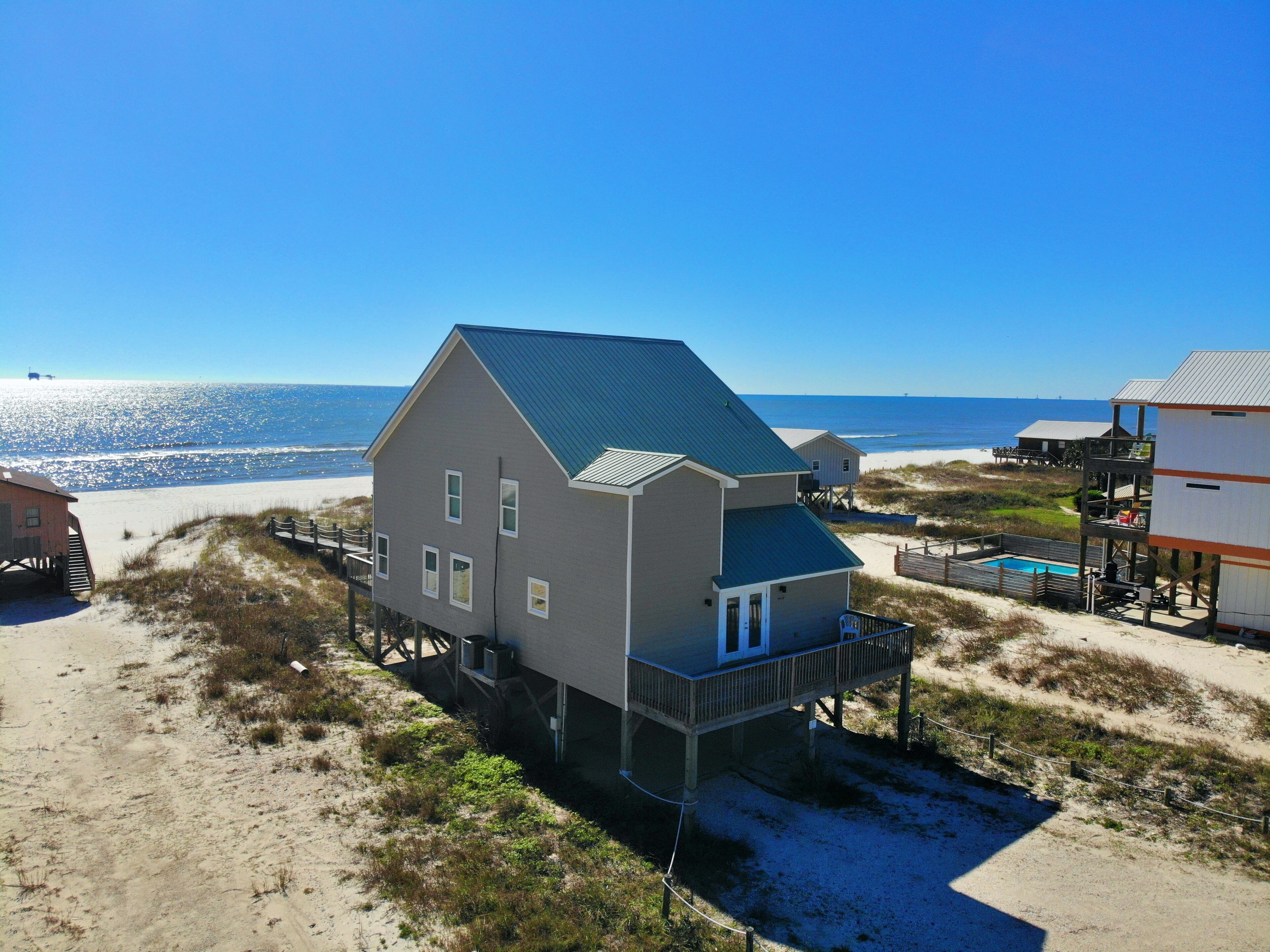 En toetages strandhus med balkon, beliggende på en sandstrand med udsigt over havet.