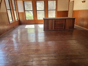 Ein Zimmer mit Holzboden, großen Fenstern und einem Holzkabinett.