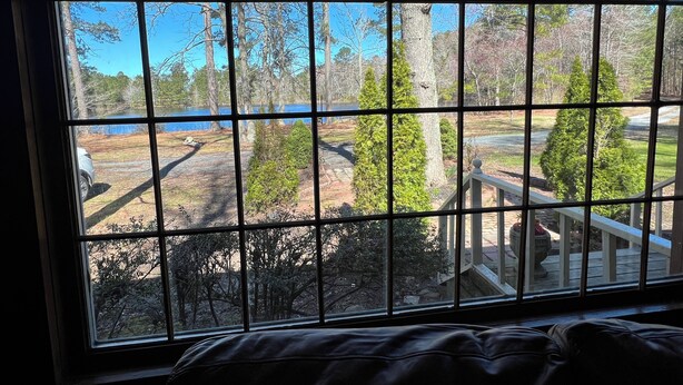 A room with a large window overlooking a lake, trees, and a wooden deck. - Peaceful Entire 4 BR 2 BA Cabin with AC, WiFi, Pond  View, Recreational room (Crisfield)