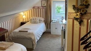A bedroom with two beds, a bedside table, a lamp, a mirror, and a window with curtains. - Regis Lodge Guesthouse  (Bognor Regis)