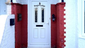 A white door with the number 3 and the name "Regis Lodge" above it, flanked by red brick walls and a white brick wall. - Regis Lodge Guesthouse  (Bognor Regis)