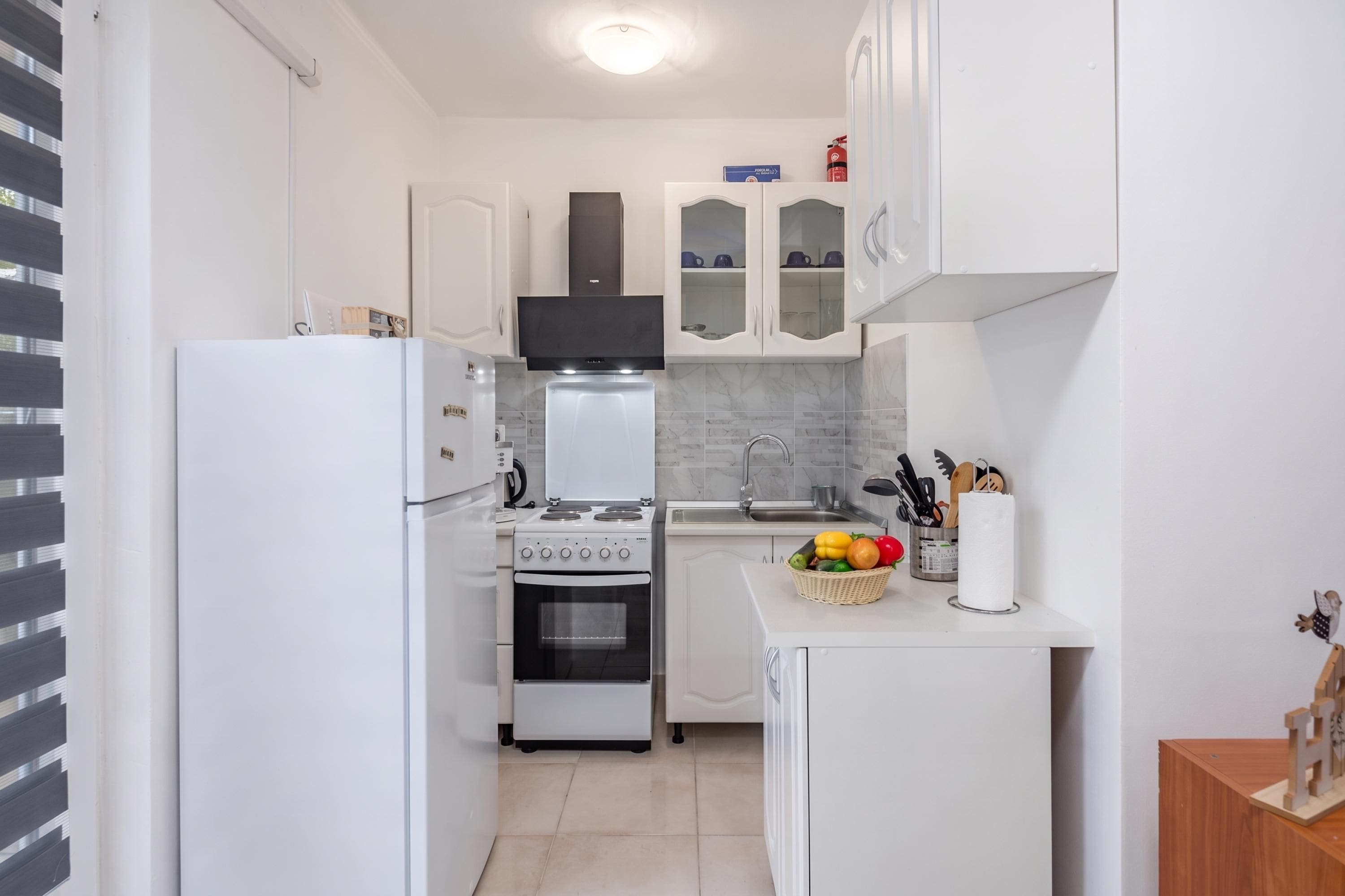 A compact kitchen with white cabinetry, a built-in oven, a stove, and a sink.