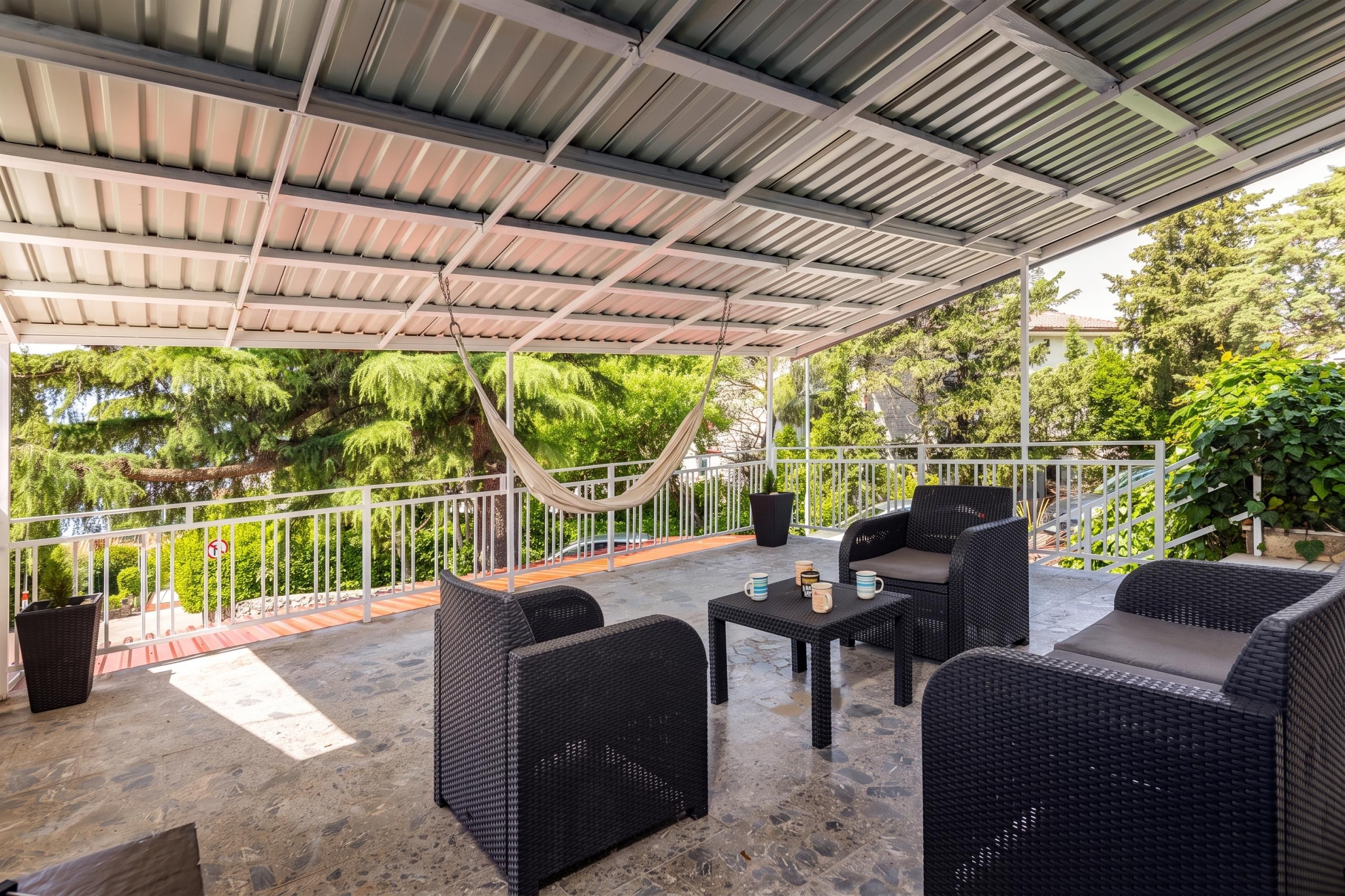 An outdoor patio with wicker furniture, a table with mugs, and a hammock.
