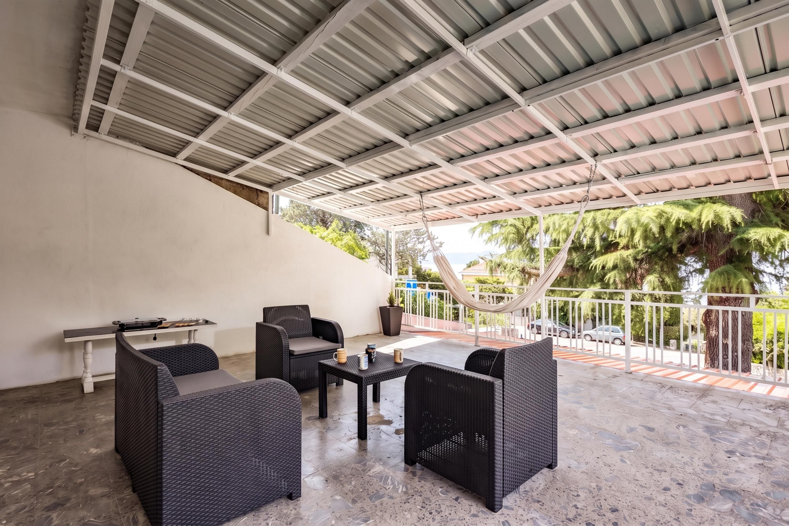 Un espacio al aire libre con mobiliario de mimbre, una mesa y una hamaca.