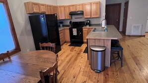Une cuisine avec des meubles de rangement en bois, un réfrigérateur noir, une cuisinière et une table à manger avec des chaises.
