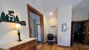 Une pièce spacieuse avec un plancher en bois, une commode en bois dotée de tiroirs, un bureau avec une chaise et une lampe fixée au mur.