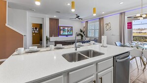 A modern kitchen with a central island, stainless steel sink, and overhead lighting. - 295 Marcello Blvd (Kissimmee)