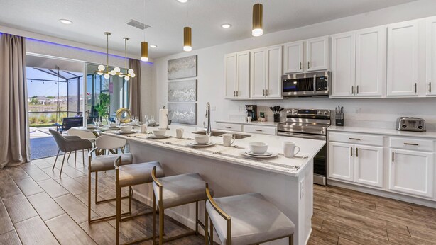 A modern kitchen with white cabinets, stainless steel appliances, and a central island with bar stools. - 295 Marcello Blvd (Kissimmee)