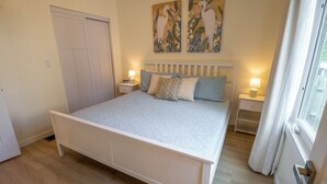 Une chambre à coucher avec un grand lit, deux tables de chevet avec des lampes, une armoire et deux tableaux accrochés au mur.