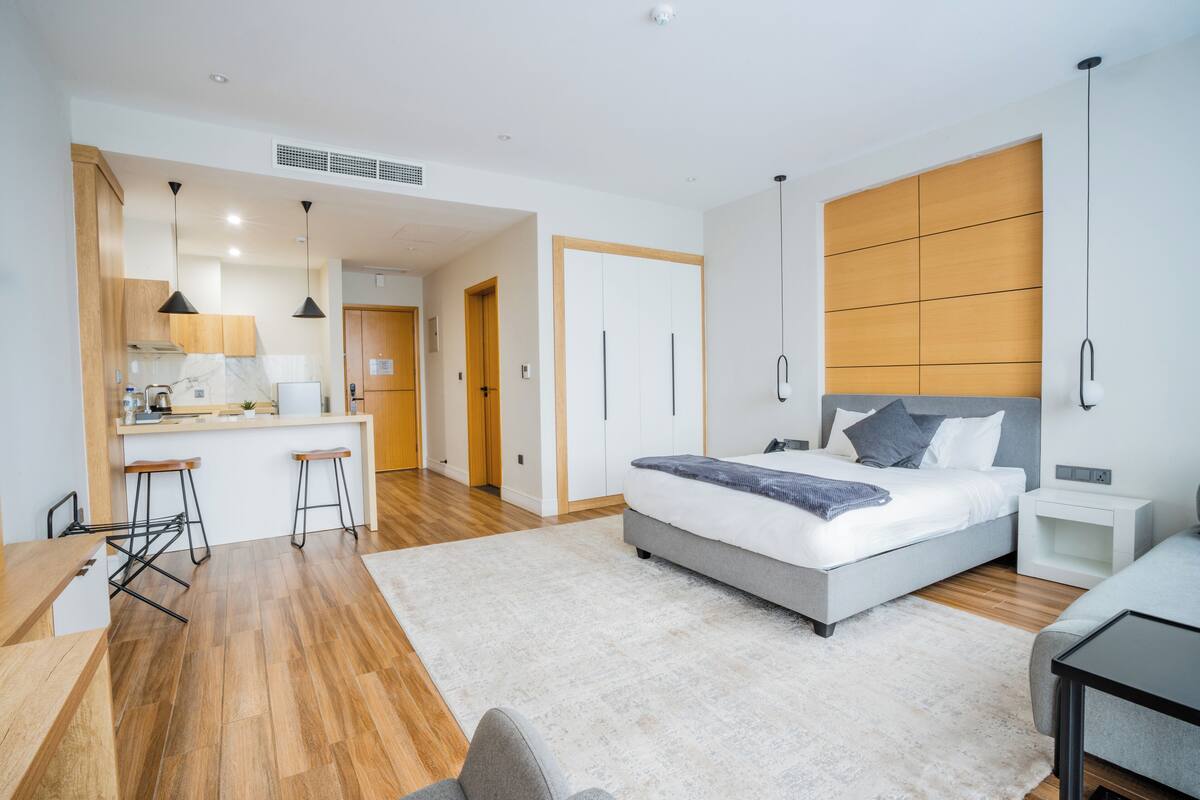 Un dormitorio moderno con una cama grande, mesitas de noche, un escritorio y una zona de cocina con taburetes.