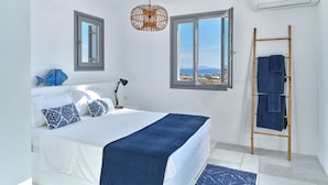 A bedroom with a bed, a desk, a lamp, a rattan light fixture, a window, and a towel rack. - Villa louise, sea view, swimming pool, sleeps 12, near Drios (Drios)