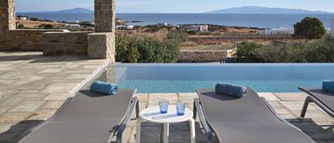 A poolside area with two sun loungers, a small table, and a stone pillar.