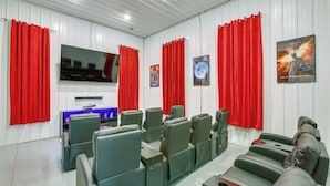 Een bioscoopkamer met meerdere zitgedeeltes, een grote flatscreen televisie en rode gordijnen.