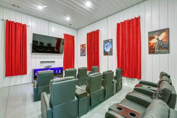 A home theater with multiple seating areas, a large flat-screen TV, and red curtains. - Group Getaway in Cadillac MI W/ Theater Room (Cadillac)