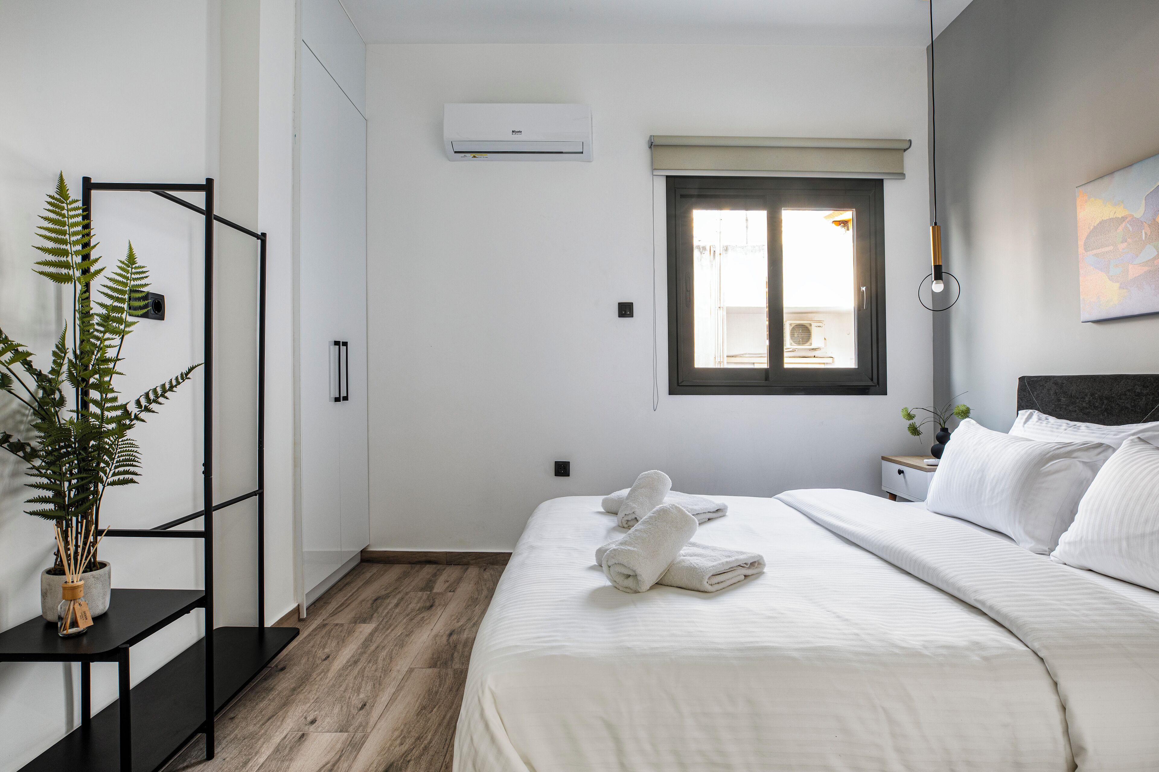 A bedroom with a bed, a potted plant, a window, and a wall-mounted air conditioner.