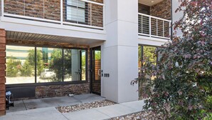 A modern building with a brick facade, large windows, and a stone pathway leading to the entrance.