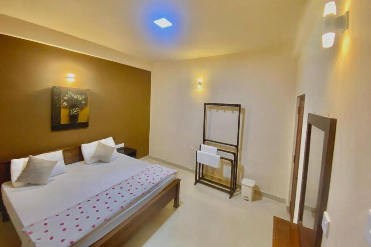 A hotel room with a bed, a bedside table, a mirror, and a wall-mounted light fixture.