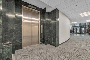 Elevator area with a control panel and glass door leading to adjacent space.
