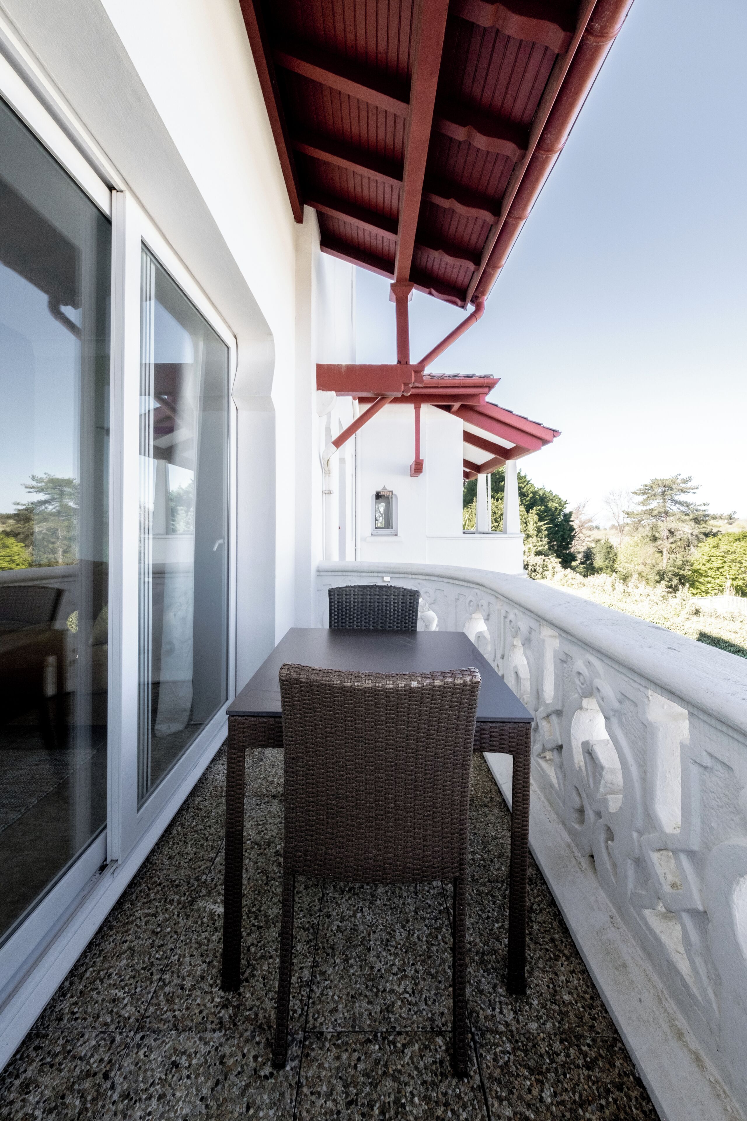 Un balcón con mesa y sillas, una puerta de vidrio y una estructura de techo roja.