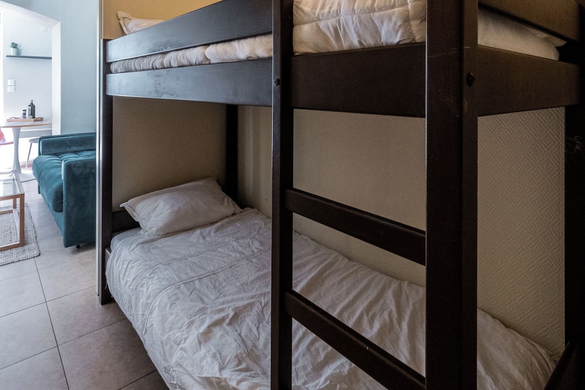 Una cama litera con ropa de cama blanca en una habitación con suelo de baldosas y una puerta que da a otra habitación.