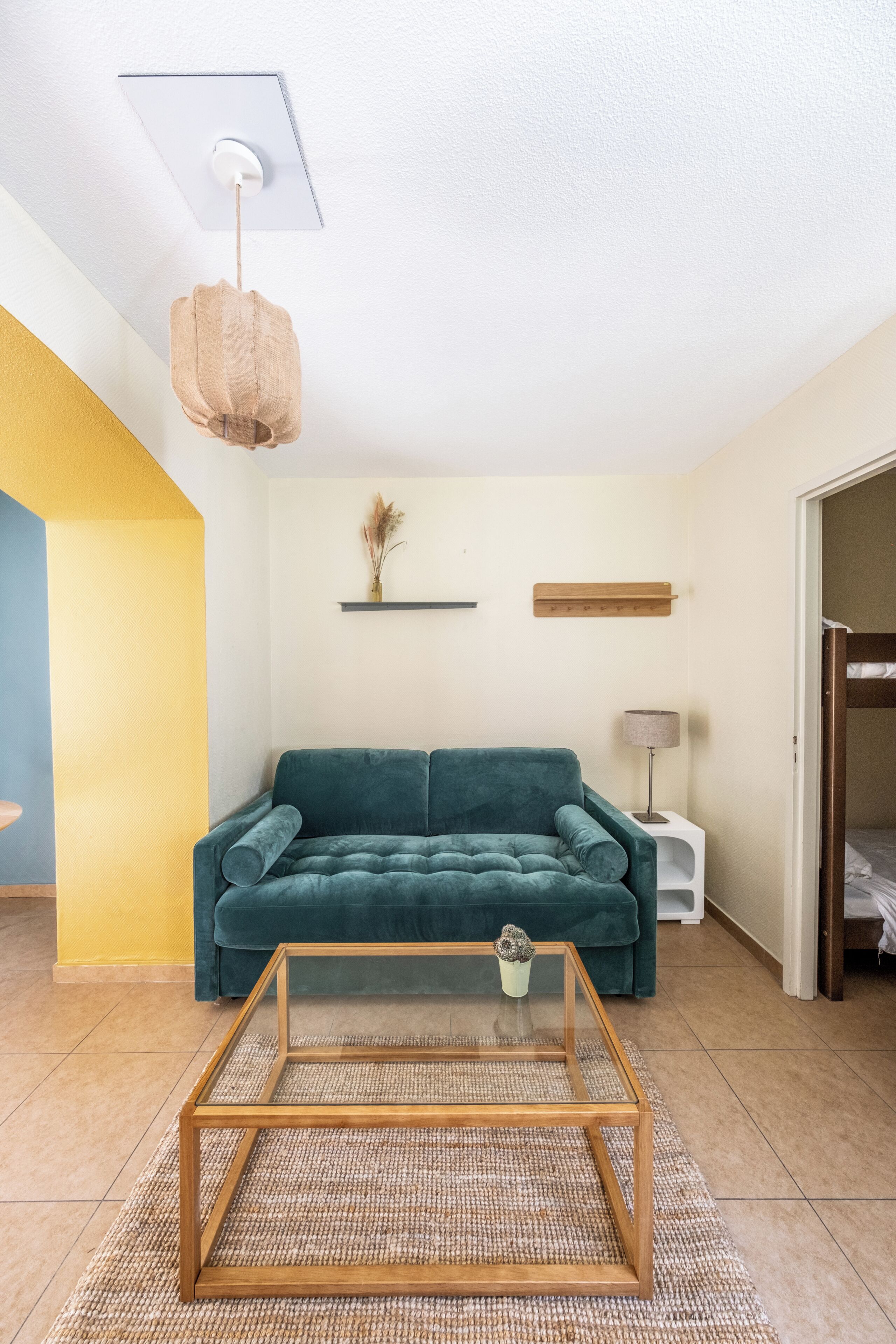 Uma sala de estar com um sofá verde-água, uma mesa de centro de vidro, uma luminária e uma estante fixada na parede.
