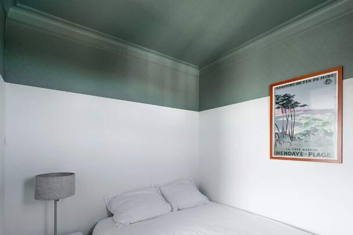 Un dormitorio con cama, mesita de noche, lámpara y un cartel en la pared.