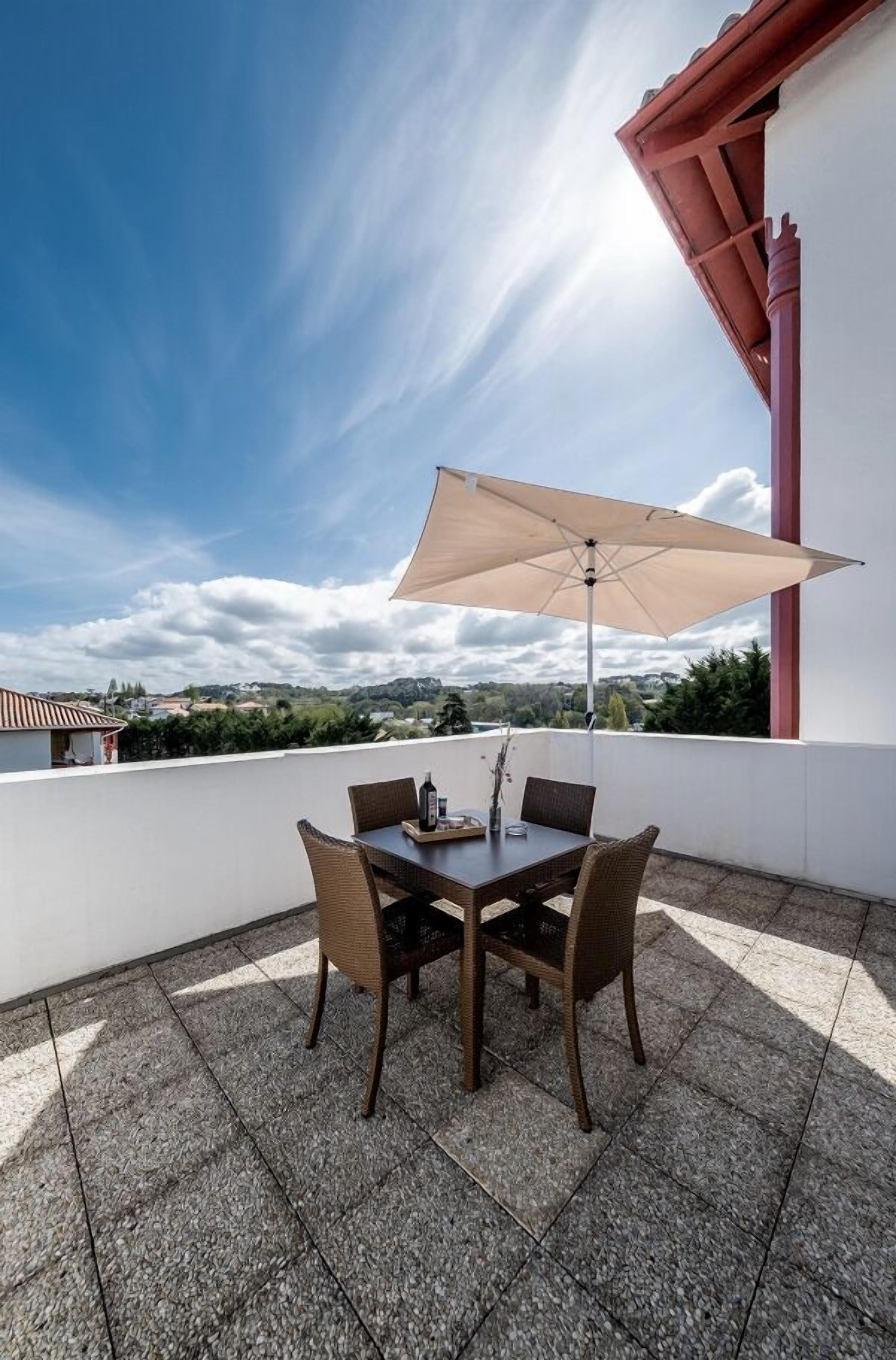 Een terras met een tafel, stoelen en een grote parasol, met uitzicht op het landschap.