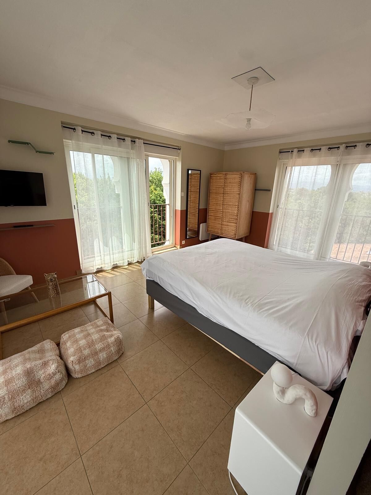 A bedroom with a large bed, a TV mounted on the wall, a balcony with a view, and a bathroom with a toilet and sink.